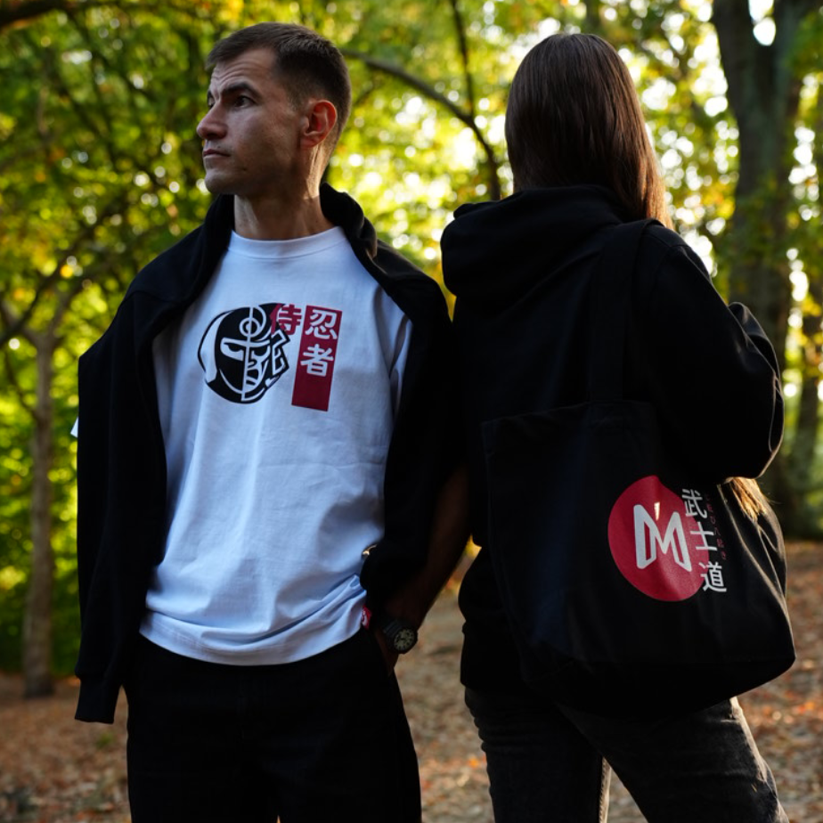 Two people standing outdoors with one wearing samuari/ ninja Bushido tee and the second model wearing Bushido Hoodie with Ikigai Tote bag.