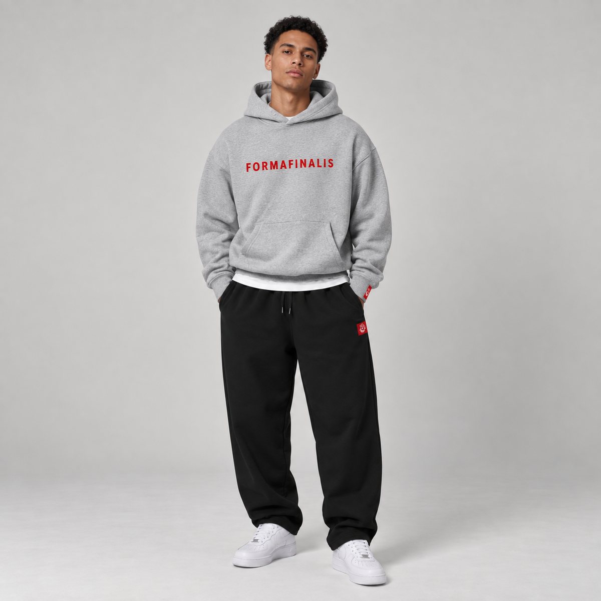 Model wearing a heather grey FF Capsule 500 GSM heavyweight cotton hoodie with red embroidered FormaFinalis wordmark and black relaxed cuffless fleece joggers.