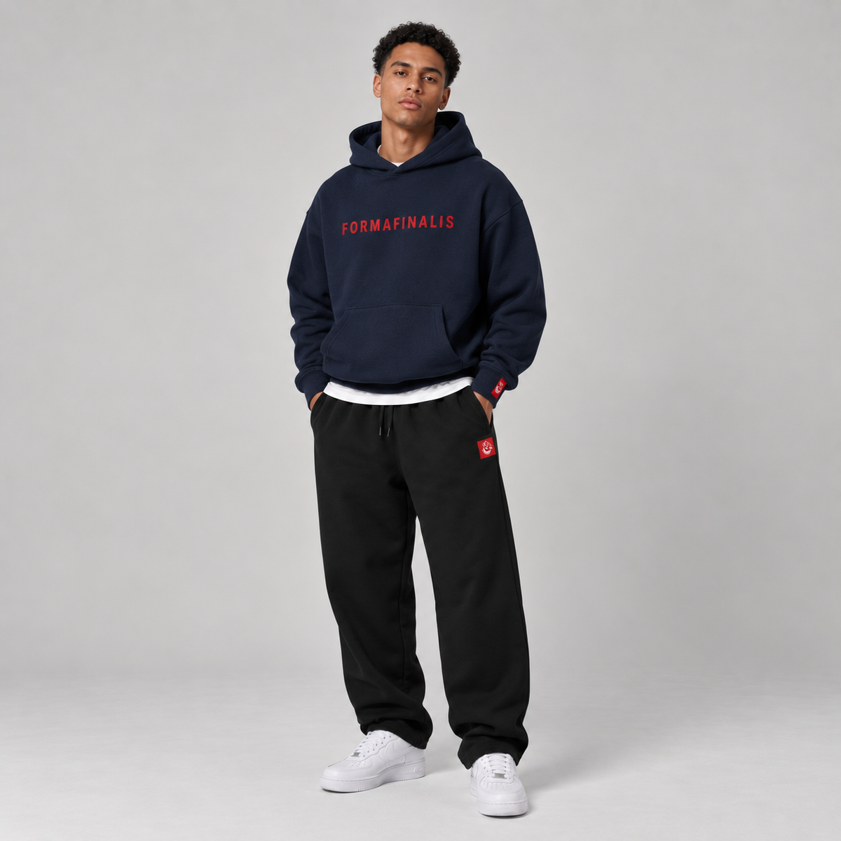 Male model wearing a navy FF Capsule 500 GSM heavyweight cotton hoodie with red embroidered FormaFinalis wordmark and black relaxed cuffless fleece joggers